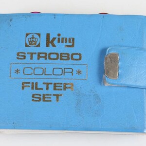 Può includere: Una custodia blu chiaro King Strobo Color Filter Set con chiusura argentata. La custodia presenta scritte dorate che recitano "STROBO *COLOR* FILTER SET". La custodia è rettangolare e ha un piccolo lembo con chiusura argentata.