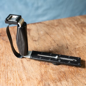 May include: Black flash bracket with a swivel arm and a hot shoe mount. The bracket has a sliding adjustment mechanism and a standard tripod mount.