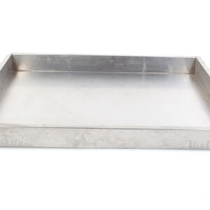 May include: A rectangular, stainless steel baking pan with a shallow depth. The pan has straight sides and a flat bottom, ideal for baking or serving. The metal has a brushed finish and reflects light.