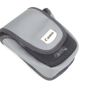 May include: A gray Canon camera case with a black mesh pocket and trim. The case has a rectangular shape with a curved top and a silver Canon logo. The case is designed to protect a camera.