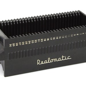 May include: Black plastic slide storage box with 30 numbered slots. The box has a rectangular shape with a handle on the side and the word "Realomatic" printed on the front.
