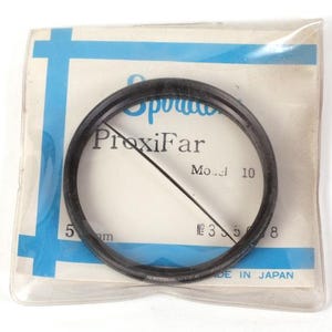 Puede incluir: Un anillo de lente ProxiFar negro, Modelo 10, en un paquete de plástico transparente. El paquete tiene detalles en azul y blanco y el texto "5 mm" y "MADE IN JAPAN".
