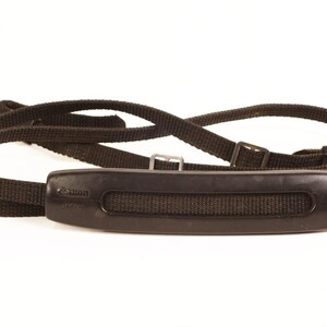 May include: Black camera strap with a padded black handle that says "Canon" on it.