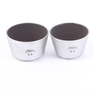 May include: Two silver-colored lens hoods with a ridged interior. The hoods are labeled "Walz" with "EB" and "BH" below the logo. The hoods have a conical shape, wider at the top and narrower at the base. They are designed to shield camera lenses from stray light.