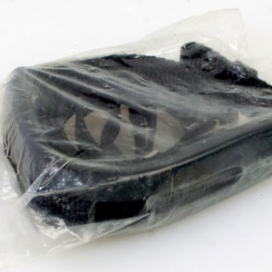 Puede incluir: Una correa de cámara negra con una hebilla plateada, empaquetada en plástico transparente.