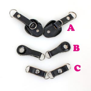 以下が含まれることがあります： 金属製のリングとハトメが付いた黒い革製のストラップループが3つあります。 上部のループは、金属製のリングで接続された2つの部分で構成されています。 中間のループは、金属製のリングとハトメが1つ付いた1つの部分で構成されています。 下部のループは、2つの金属製のリングで接続された2つの部分で構成されています。