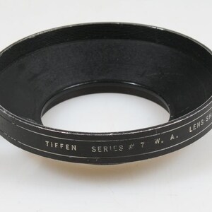 May include: A black Tiffen Series #7 W.A. lens shade. The lens shade is circular with a textured interior and a slightly worn exterior. The words "TIFFEN SERIES # 7 W. A. LENS SHADE" are printed on the exterior.