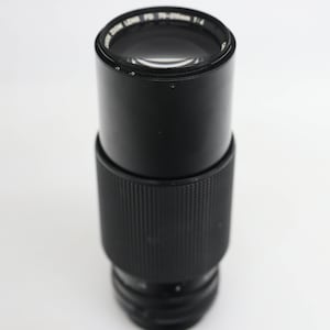 May include: A black Canon FD 200mm f/4 lens with a silver ring around the front element.