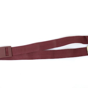 May include: A maroon adjustable strap with gold metal hardware and two D-rings.