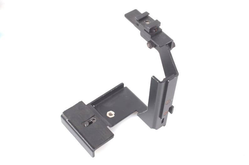 Op de afbeelding: Zwart metalen camera-accessoire met een montagebeugel en verstelbare arm. Het accessoire heeft een rechthoekige basis en een verticale arm met een flitsschoen. Het is ontworpen om aan een camera te bevestigen.