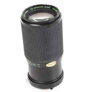 May include: Black zoom lens with green and white text, including "75-200mm 1:4.5 MACRO". The lens has a textured grip and a "PASSED" sticker. A photography accessory.