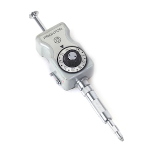 May include: A gray Prontor camera shutter release cable with a black circular dial featuring white numbers from 4 to 32. The device has a metallic silver plunger at the top and a textured silver cylindrical connector at the bottom end.