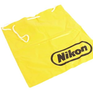 May include: A bright yellow drawstring bag with the word "Nikon" printed in black.