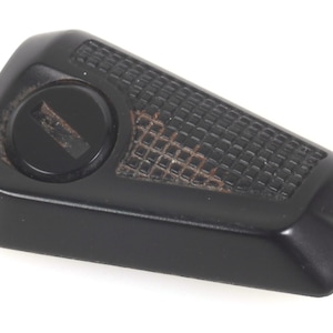 May include: A black plastic component with a textured surface and a circular recess. The object features a grid-like pattern and a small, circular indentation. It is likely a part of a larger mechanism or device.