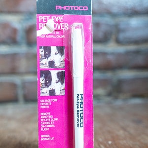 Könnte beinhalten: Eine pinkfarbene und weiße Verpackung mit einem weißen Stift, der mit "Photoco Pet-Eye Remover" beschriftet ist. Die Verpackung zeigt Vorher- und Nachher-Fotos von Hundenaugen, die die Fähigkeit des Produkts demonstrieren, rote Augen von Fotos zu entfernen. Die Verpackung enthält auch den Text "Retten Sie Ihre Lieblingsdrucke!" und "Entfernen Sie störendes Tieraugen-Glimmen, das durch den Blitz der Kamera verursacht wird!"