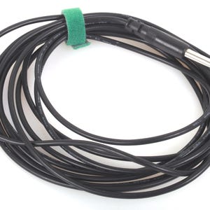 May include: A coiled black audio cable secured with a green velcro strap. The cable features a 6.35 mm male connector at one end and a smaller connector at the other. The cable is against a white backdrop.