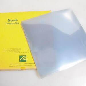 May include: A yellow box labeled "Seal Transpara-Film" with a clear, transparent sheet of film next to it. The box has green and black text and a logo. The film appears to be a large, square sheet.