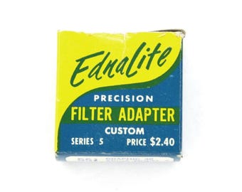 May include: A small, vintage box for an Ednalite precision filter adapter. The box is primarily yellow and blue, with the words "Ednalite" in green script. The text "Filter Adapter" is prominently displayed. The box is labeled "Series 5".