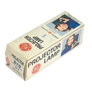 May include: Vintage General Electric projector lamp box. The rectangular box is off-white with red and black text and a GE logo. The box features an image of a woman holding a phone. The box reads "PROJECTOR LAMP" and "20 V 100 Watts."
