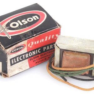 May include: A vintage Olson Electronic Parts transformer and its original box. The box is black with red and white details. The transformer has copper and wire components. The box reads "Quality Electronic Parts" and "Olson".