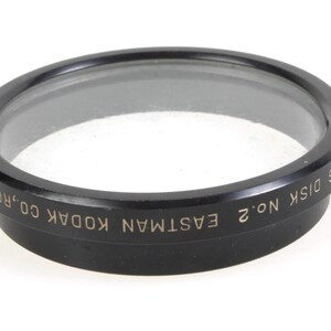 May include: Black circular filter holder with the text "EASTMAN NO. 2 DISK  KODAK CO. ROCHESTER" in gold lettering.