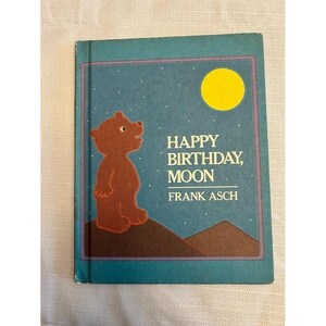 May include: A children's book titled "Happy Birthday, Moon" by Frank Asch. The cover features a brown bear, a yellow moon, and the title text against a blue night sky background. The book has a teal border.
