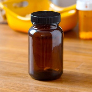 May include: A dark brown glass bottle with a black lid. The bottle is empty and sitting on a wooden surface.