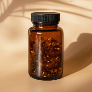May include: A brown glass bottle with a black lid filled with clear capsules. The bottle is sitting on a light brown surface.