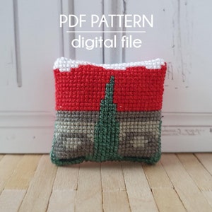 Könnte beinhalten: Ein kleines, rot, grün und graues Kreuzstich-Kissen mit einer weißen, schneebedeckten Oberseite. Das Kissen liegt auf einer Holzoberfläche. Der Text "PDF PATTERN digital file" befindet sich über dem Kissen.