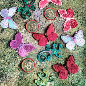 Könnte beinhalten: Sortiment an bunten, gestickten Bügelbildern mit Schmetterlingen, Eidechsen und dem Symbol Om. Die Patches sind perfekt, um Kleidung, Taschen oder anderen Stoffartikeln einen Hauch von Verspieltheit zu verleihen.