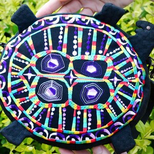 May include: A black turtle-shaped bag with colourful embroidered details. The embroidery features a geometric pattern with purple, green, yellow, red and white thread.