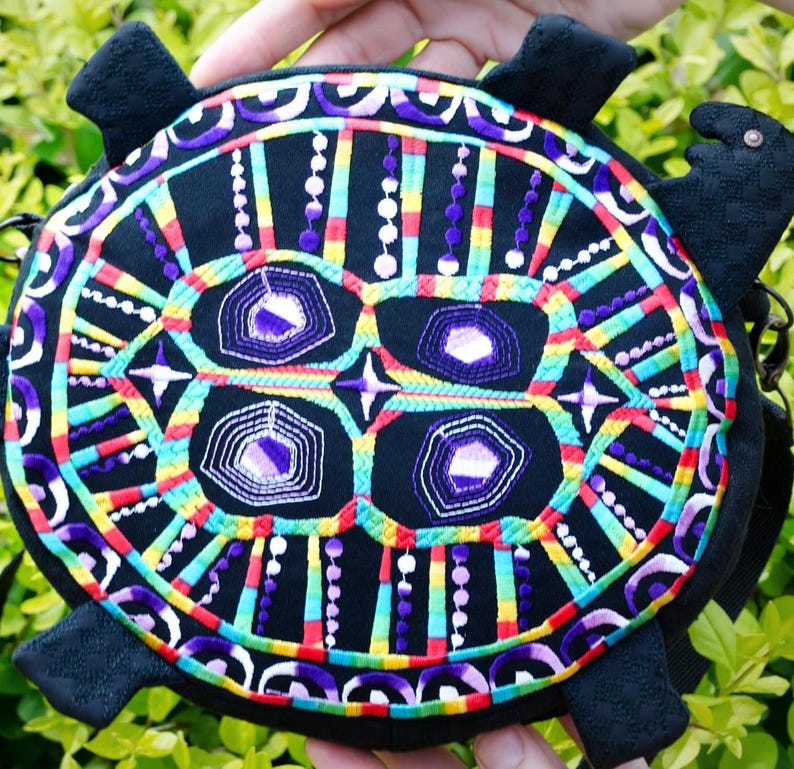 May include: A black turtle-shaped bag with colourful embroidered details. The embroidery features a geometric pattern with purple, green, yellow, red and white thread.