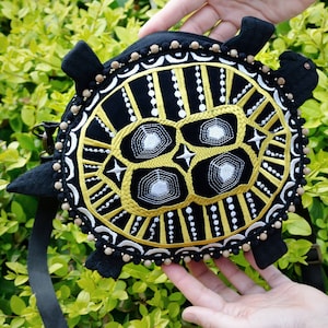 May include: A black turtle-shaped purse with a gold and white embroidered design. The purse has a black strap and a beaded trim.