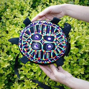 May include: A black turtle-shaped purse with a colourful embroidered design. The embroidery features a geometric pattern with purple, red, yellow, green, and blue accents.