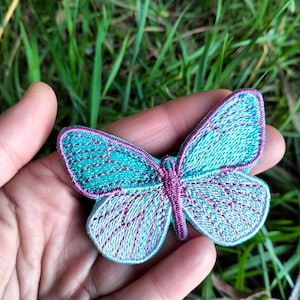 May include: A teal and purple embroidered butterfly patch. The butterfly has a light blue and white gradient on the wings.