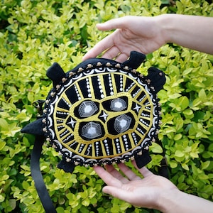 May include: A black and gold embroidered turtle-shaped purse with a black strap. The purse has a geometric design with white accents.