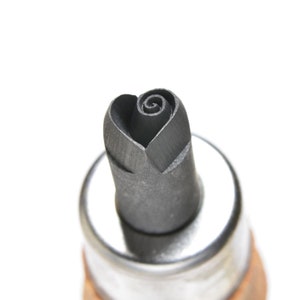 May include: Close-up of a metal stamp with a rose design. The stamp head is shaped like a rose with a spiraling center. The metal is a dark gray color, and the handle is visible at the bottom.