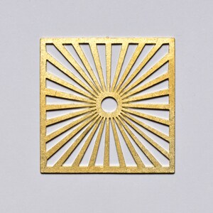 May include: A gold metal square with a sunburst design. The centre of the square has a circle cut out.