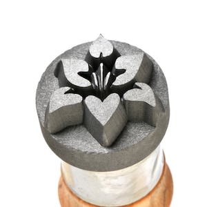 May include: A close-up of a metal stamp with a floral design. The stamp is round and has a gray finish. The design features a stylized flower with five petals and a heart in the center.