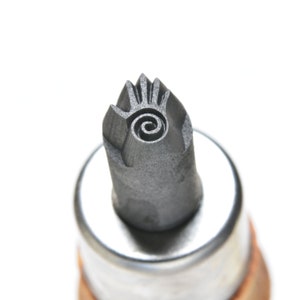 May include: A close-up of a metal tool with a spiral design and a hand-shaped impression. The tool is attached to a wooden handle.