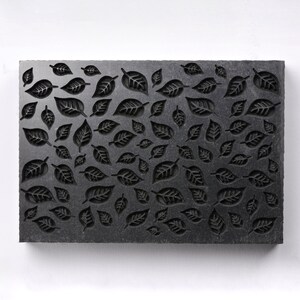 May include: A black slate tile with a repeating pattern of carved leaf shapes.
