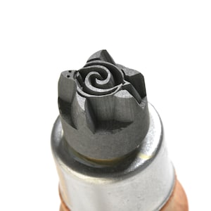 May include: A close-up of a black metal stamp with a detailed floral design. The stamp is attached to a wooden handle.