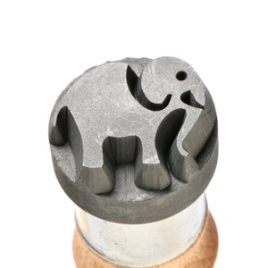May include: A gray metal stamp with an elephant design. The stamp is mounted on a wooden handle.