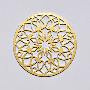 May include: A gold-coloured metal ornament with a circular design featuring a starburst pattern and intricate cutouts.