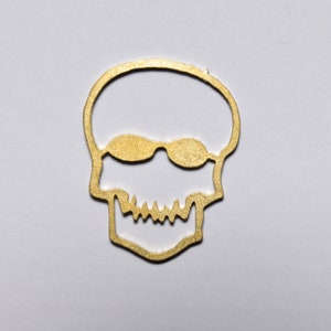 May include: A gold-coloured metal skull cutout with a pair of sunglasses.
