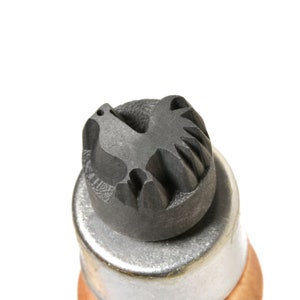 May include: A close-up of a black metal stamp with a dove design. The stamp is mounted on a silver metal base.