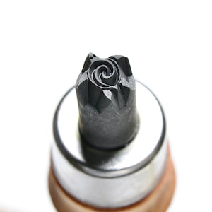 May include: A close-up of a black metal stamp with a spiral design. The stamp is mounted on a silver base with a wooden handle.