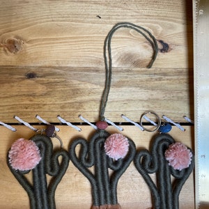 May include: Three green string cactus keychains with pink pom poms and brown tassels. Each keychain has a small lava rock bead and a silver key ring.