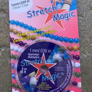 Könnte beinhalten: Eine Rolle durchsichtiges, elastisches Stretch-Perlen- und Schmuckband, 1 mm im Durchmesser, 5 Meter oder 16 Fuß lang. Die Verpackung ist rosa und zeigt einen roten Stern mit den Worten "Stretch Magic" und "Bead & Jewelry Cord".