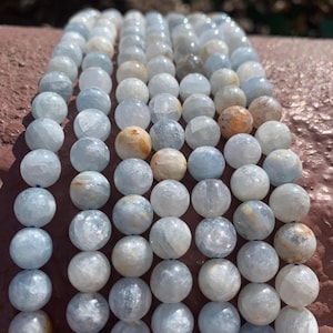 May include: A strand of light blue, white, and brown gemstone beads. The beads are round and have a smooth, polished finish.